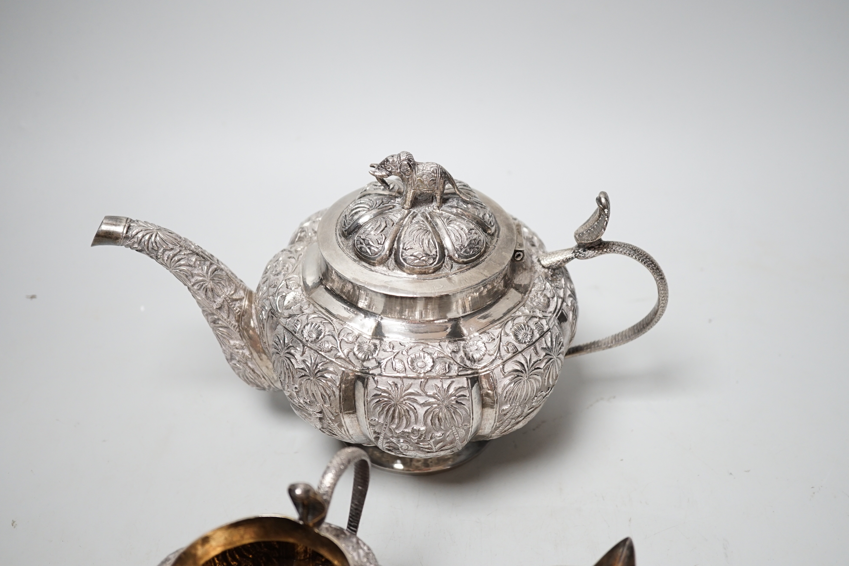 An Indian embossed white metal three piece tea set, with cobra handles and elephant finial, 25.7oz.